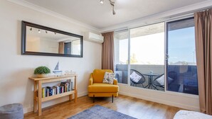 Una camera da letto moderna con una grande finestra, un divano, un comodino con libri e uno specchio.