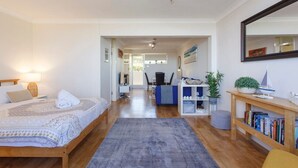 Una camera da letto moderna con un letto, un comodino e uno specchio grande. Si apre su un corridoio che conduce a un soggiorno con un divano e un tavolino.