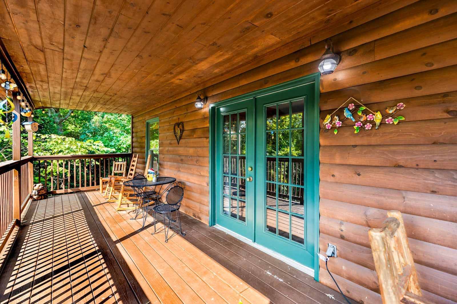 A wooden cabin with a covered porch, a table with chairs, and a green door.