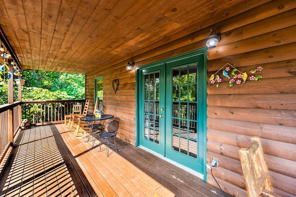 A wooden cabin with a covered porch, a table with chairs, and a green door.