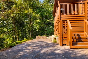 A wooden cabin with a staircase leading to a deck, surrounded by dense forest.