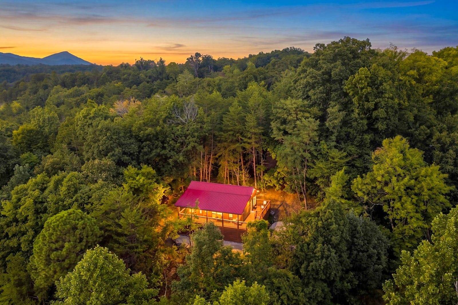 A cabin surrounded by dense forest with a red roof, accessible via a wooden deck.