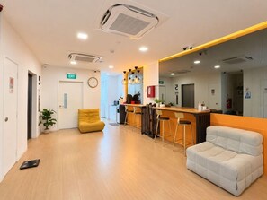 A modern interior with a reception desk, bar stools, a sofa, and a clock on the wall. - Dash Living on Mackenzie (Singapore)