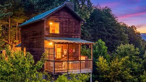 A two-story wooden cabin with a balcony, surrounded by dense forest. - Mountain Romance - Mountain Views & Hot Tub (Sevierville)