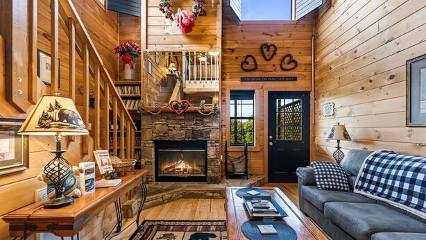 A cozy cabin interior with a fireplace, wooden walls, a staircase, and a couch. - Mountain Romance - Mountain Views & Hot Tub (Sevierville)