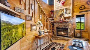 A cabin interior with a fireplace, a television, a staircase, and a scenic view. - Mountain Romance - Mountain Views & Hot Tub (Sevierville)