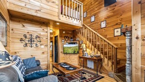 A wooden interior with a sofa, a table, a TV, and a staircase. - Mountain Romance - Mountain Views & Hot Tub (Sevierville)