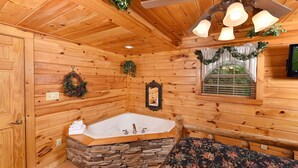 Un baño de cabaña de madera con una bañera de piedra, paredes de madera, un espejo y una ventana con vistas.