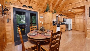 Interior de una cabaña de madera con comedor, cocina y una puerta que da al exterior.