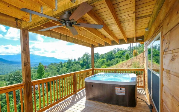 A wooden deck with a hot tub, a ceiling fan, and a view of a mountainous landscape. - Breathtaking mountain views! June discounts available! - Birdhouse - (Gatlinburg)