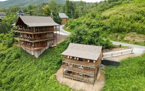 A wooden cabin with a balcony and a smaller attached building, surrounded by lush greenery and a winding road. - Breathtaking mountain views! June discounts available! - Birdhouse - (Gatlinburg)