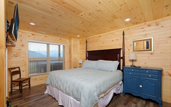 A wooden-paneled bedroom with a bed, a nightstand, a chair, and a TV mounted on the wall. - Breathtaking mountain views! June discounts available! - Birdhouse - (Gatlinburg)