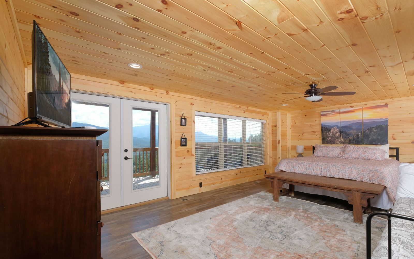 A wooden cabin bedroom with a bed, a TV, and a large window.