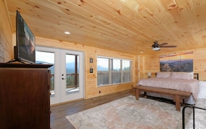 Une chambre dans une cabane en bois, avec un lit, une télévision et une grande fenêtre.
