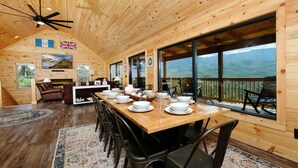 Una cabaña de madera con comedor, chimenea y grandes ventanales con vistas a la montaña.