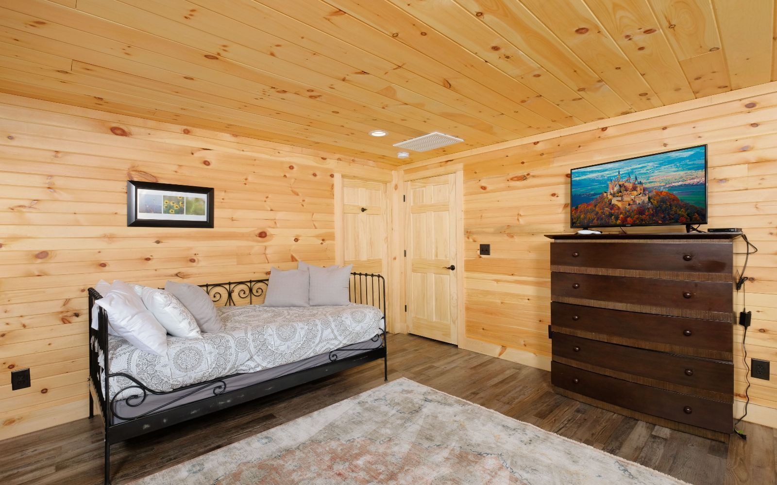 Una habitación acogedora con una cama, un aparador y un televisor en una pared de madera.
