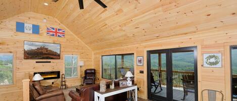 Interior acogedor de una cabaña de madera con chimenea, sofá de cuero y un balcón con vistas panorámicas.