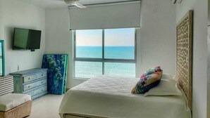 A bedroom with a bed, a dresser, a television, and a window with a view of the ocean. - Lujoso Apartamento Frente al Mar (Coveñas)