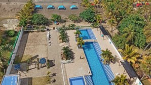 A beachside hotel with a swimming pool, beach umbrellas, and palm trees. - Lujoso Apartamento Frente al Mar (Coveñas)