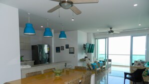 A modern kitchen with a built-in refrigerator, a dining area with a wooden table and wicker chairs, and a balcony with a view. - Lujoso Apartamento Frente al Mar (Coveñas)