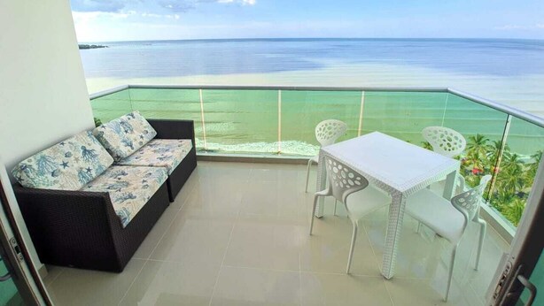 A balcony with a sofa and table, overlooking a calm sea and distant land. - Lujoso Apartamento Frente al Mar (Coveñas)