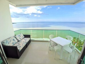 Un balcon avec un canapé et une table, offrant une vue sur une mer calme et une terre lointaine.