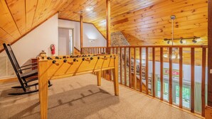 Ein gemütliches Zimmer mit Holzboden, einem Kicker und Blick auf einen Balkon mit einem Coca-Cola Schild.