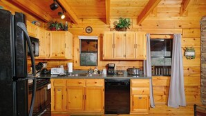A wooden cabin kitchen with a refrigerator, stove, microwave, coffee maker, and dishwasher.
