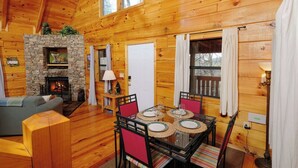 A cozy cabin interior with a stone fireplace, wooden walls, a dining table with chairs, and a sofa.