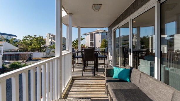 Une véranda avec une terrasse en bois, un coin salon comprenant un canapé et des fauteuils, et de grandes fenêtres offrant une vue sur le quartier.