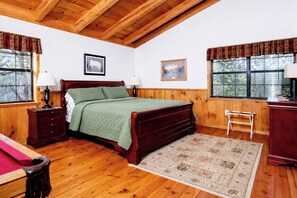 A wooden-paneled bedroom with a bed, two nightstands, a desk, and a chair.