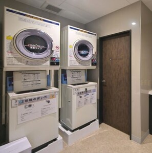 Une buanderie équipée de deux machines à laver et deux sèche-linge superposés, une porte et un sol recouvert de moquette.