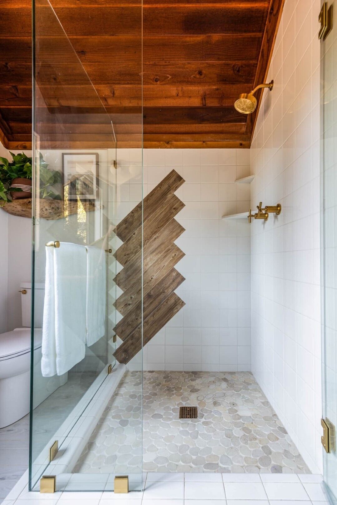 Une salle de bain moderne avec une douche à parois de verre, des éléments décoratifs en bois sur les murs et un sol carrelé en pierre.
