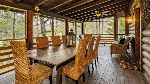 A wooden deck with a dining table and wicker chairs, surrounded by log walls and large windows.