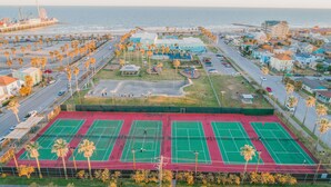 Eine Küstenlandschaft mit einem großen Tennisplatzkomplex, einem Pier mit einem Schiff und Wohnhäusern.