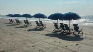 Ein Strand mit Reihen von Liegestühlen und blauen Sonnenschirmen.
