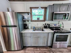 Una cocina compacta con electrodomésticos de acero inoxidable, encimera de granito y ventana con vistas a la vegetación.