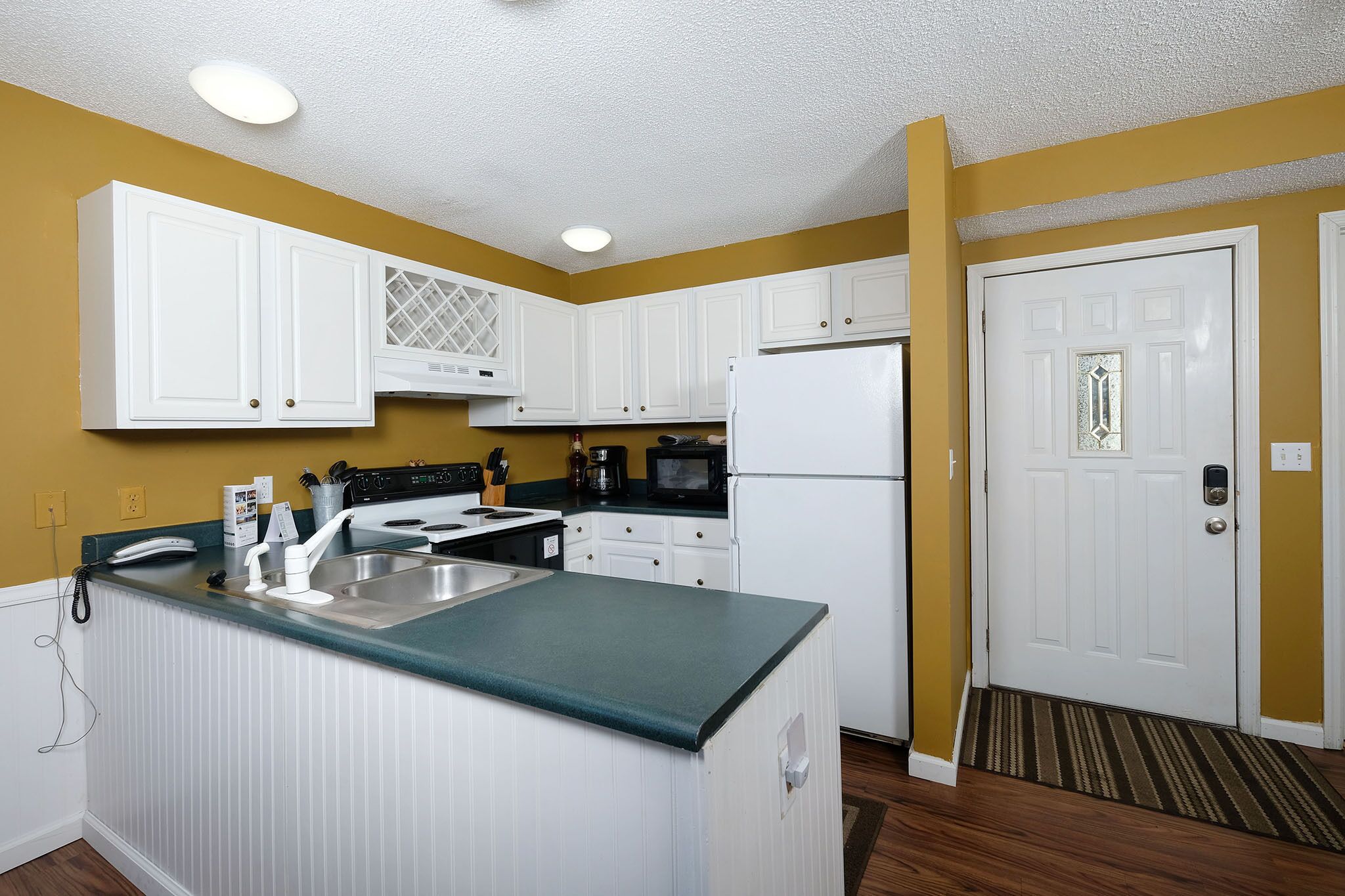 Una cocina compacta con armarios blancos, una isla integrada, un microondas y un refrigerador.
