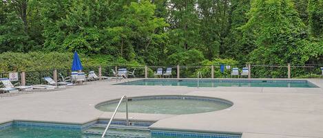 A swimming pool with lounge chairs and umbrellas, surrounded by trees.