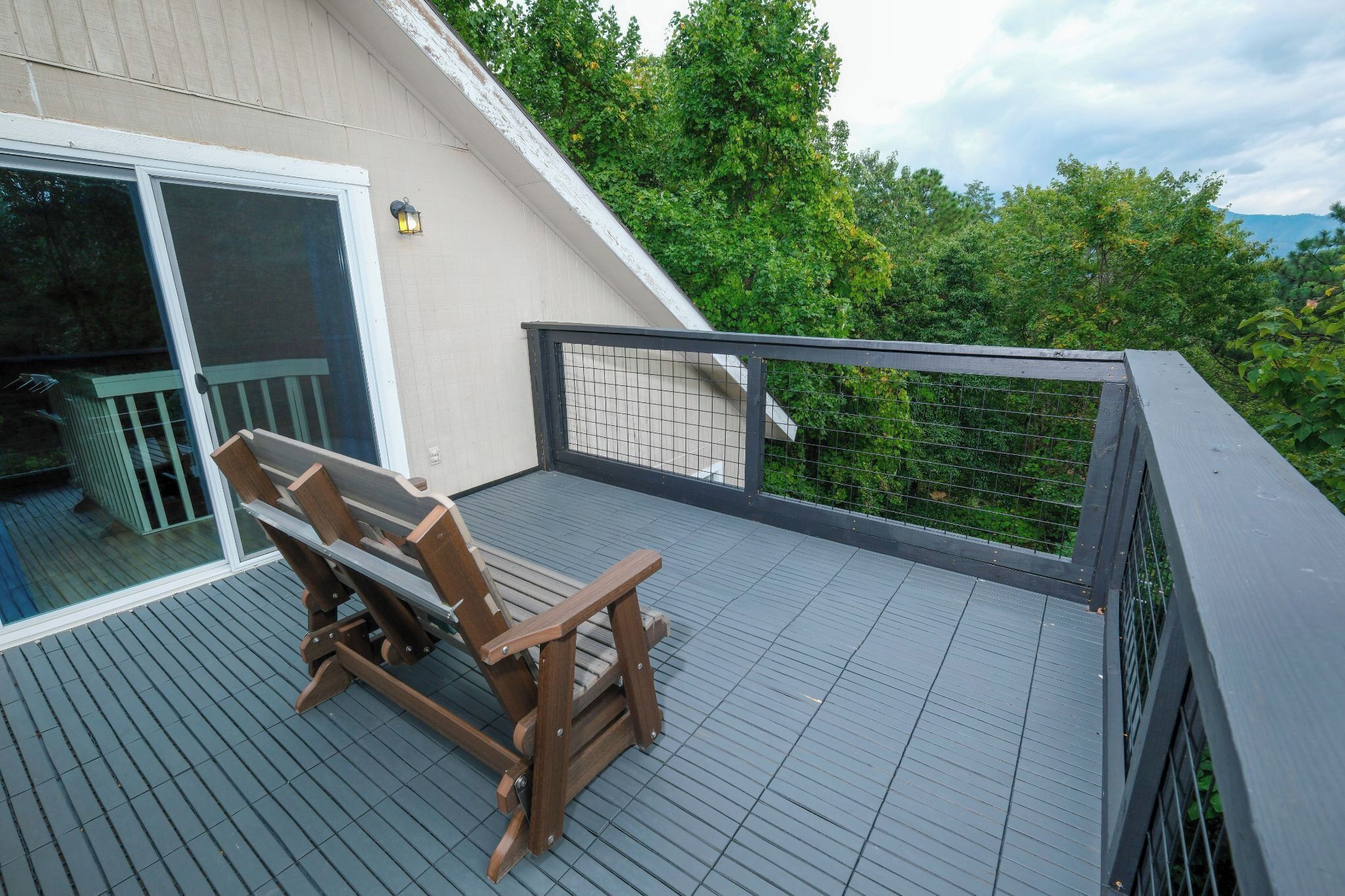 Eine Holzterrasse mit einer Bank, einer Glastür und einem Geländer mit Blick auf eine üppige, grüne Landschaft.
