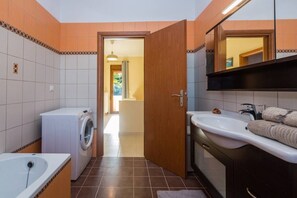 A compact bathroom with a washing machine, a sink, and a mirror.