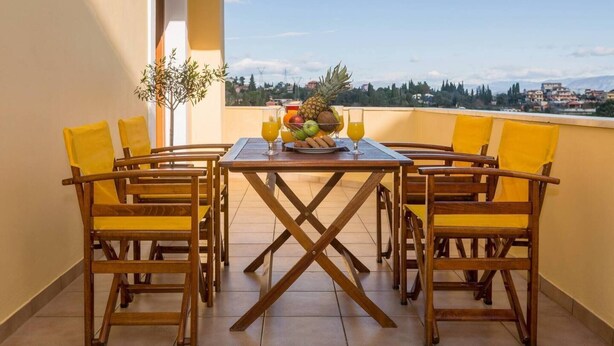 A balcony with a wooden table and four yellow chairs, a fruit bowl, and two glasses of orange juice. - Louisa's Summer House (Corfu)