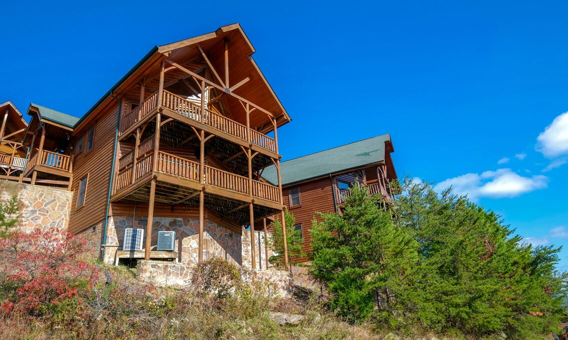 A wooden cabin with a stone foundation, multiple balconies, and a view of the surrounding landscape.