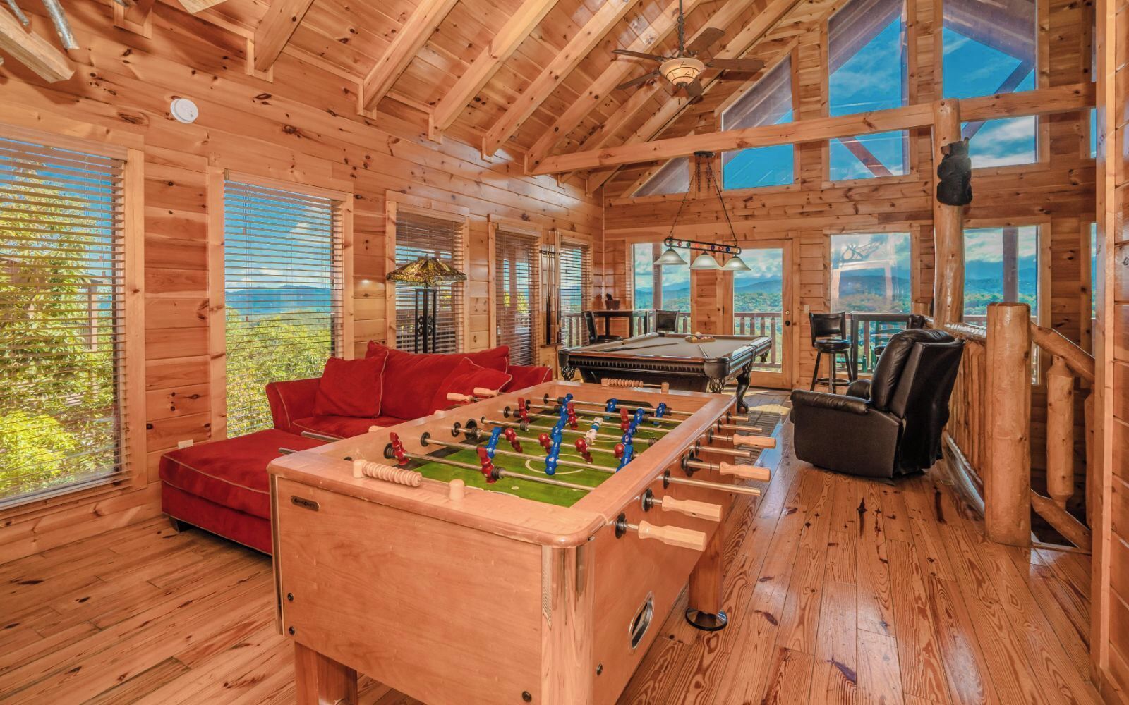Une chaleureuse cabane en bois avec un baby-foot, un canapé rouge et une table de billard.