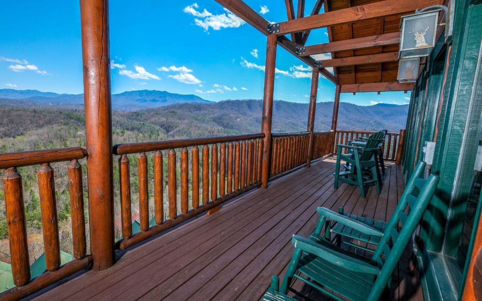 A wooden deck with chairs and a railing overlooking a mountainous landscape.
