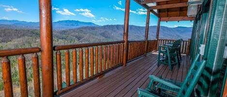A wooden deck with chairs and a railing overlooking a mountainous landscape.