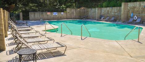 A swimming pool with lounge chairs and a table, surrounded by a concrete deck and a wooden fence.
