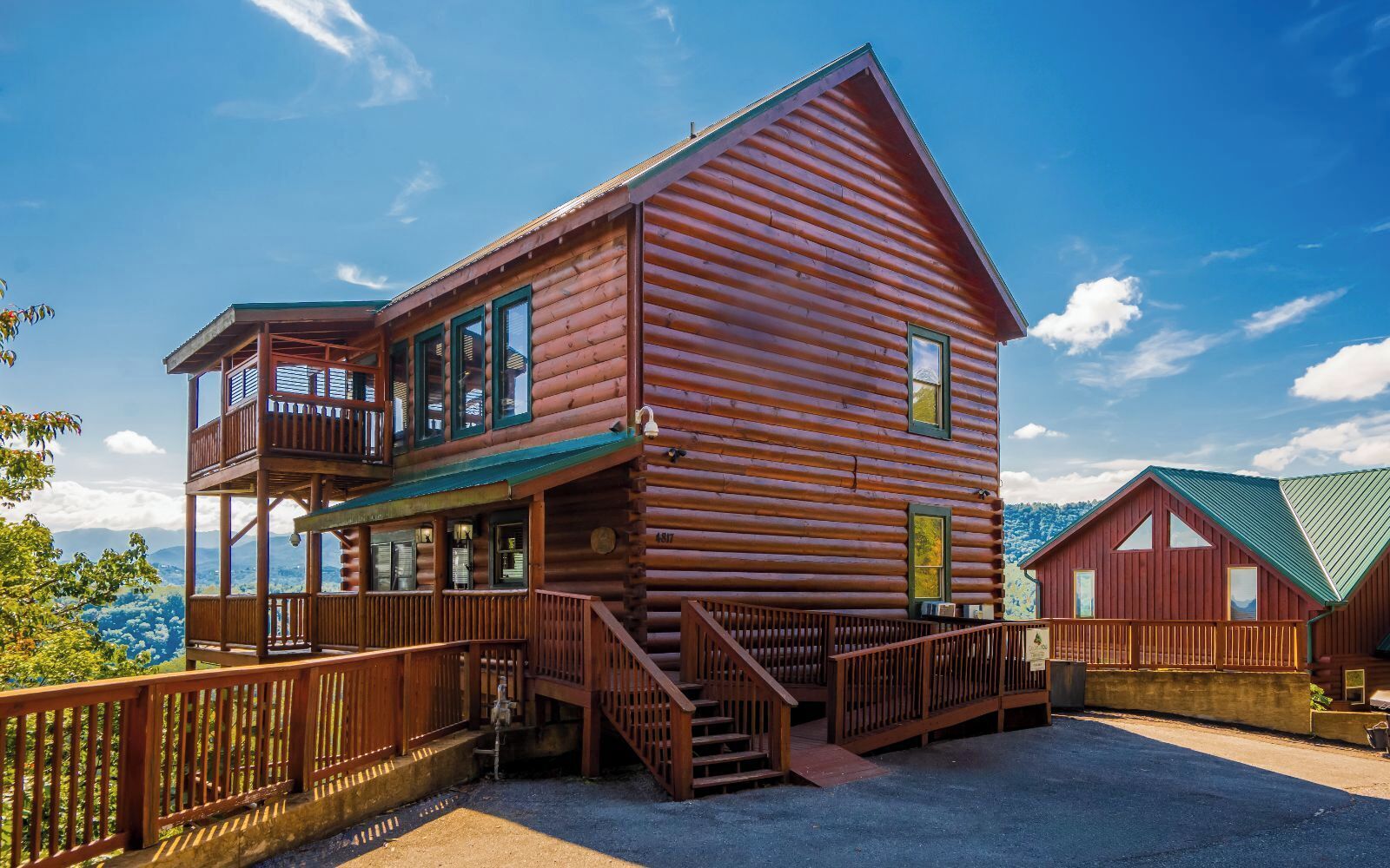 A two-story log cabin with a balcony and a covered porch, surrounded by a wooden fence.