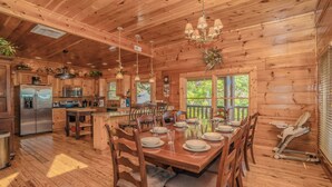 Interior de una cabaña de madera con comedor, cocina y vista al exterior.
