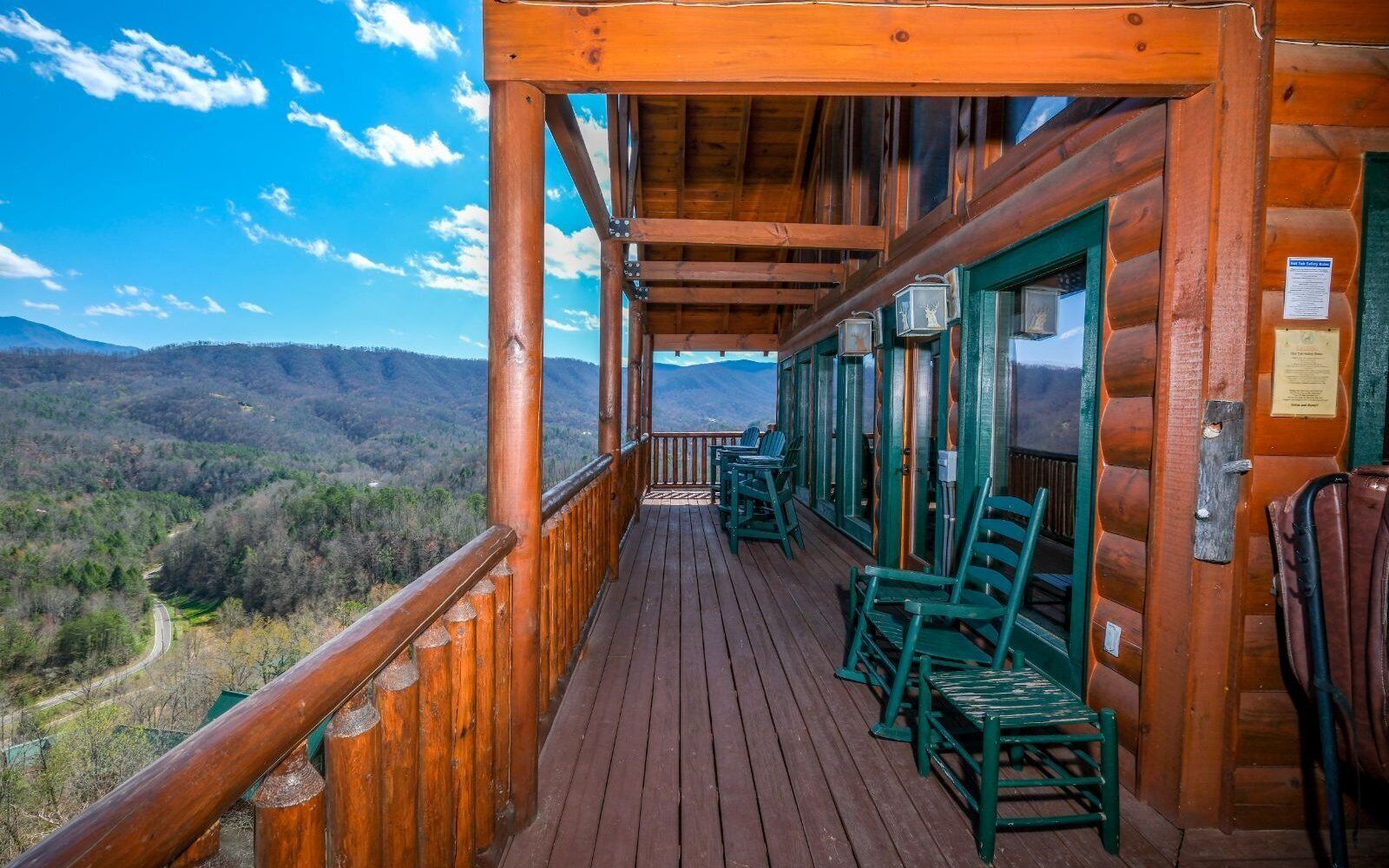 A wooden deck with chairs, a view of a valley, and mountains in the distance.